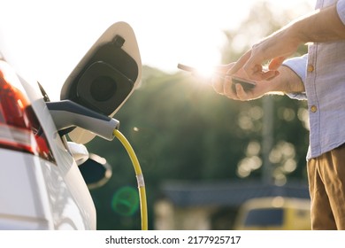 Male unplugging in power cord to electric car using app on smartphone. Businessman charging electric car at outdoor charging station Unrecognizable man unplugging electric car from charging station. - Powered by Shutterstock