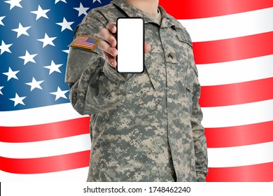 Male In US Army Soldier (ISAF) Uniform Holding Black Smartphone With Isolated White Screen. Flag Of USA On Background. (different Version)