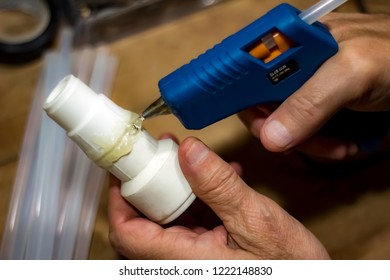 Male Using Glue Gun To Fix A Plastic Pipe Part