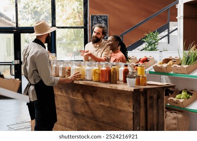 Male vendor offering advice to clients who are shopping for sustainable merchandise at eco friendly store. Owner of local supermarket describing food items in jars to the young multiracial couple. - Powered by Shutterstock