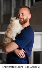 Male Veterinarian Holds Dog In His Arms And Laughs, Dog Licks People Face.