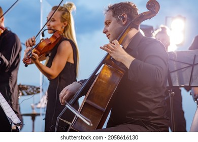 Male violoncellist playing in orchestra at outdoor concert - Shutterstock ID 2058616130