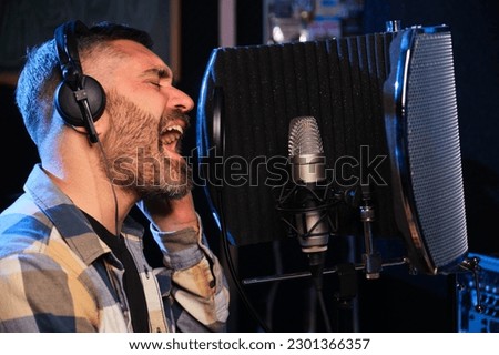 Male vocal artist, singer, with headphones recording new album at a recording studio.