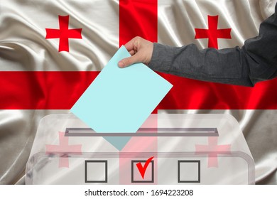 Male Voter Drops A Ballot In A Transparent Ballot Box Against The Background Of The National Flag Of Georgia, Concept Of State Elections, Referendum