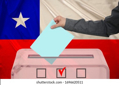 Male Voter Drops A Ballot In A Transparent Ballot Box On The Background Of The National Flag Of Chile, Concept Of State Elections, Referendum