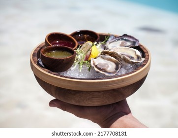 A Male Waiter Holds A Serving Of Oysters In A Beach Club. Looking Fresh And Appetizing 