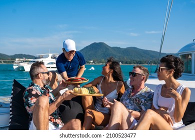 Male waiter serving fresh fruit to tourist while catamaran boat sailing in the sea in sunny day. Man and woman friends relax and enjoy luxury outdoor lifestyle sail yacht on summer travel vacation