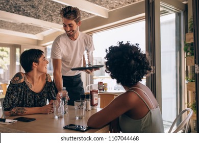 Male waiter serving water to women at cafe. Female friends at a restaurant with waiter serving water.