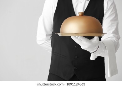 Male waiter with tray and cloche on grey background