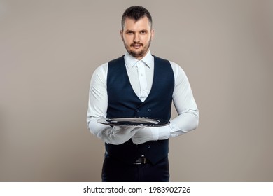 A male waiter in a white shirt and white gloves stands with a silver tray. The concept of service personnel serving customers in a restaurant