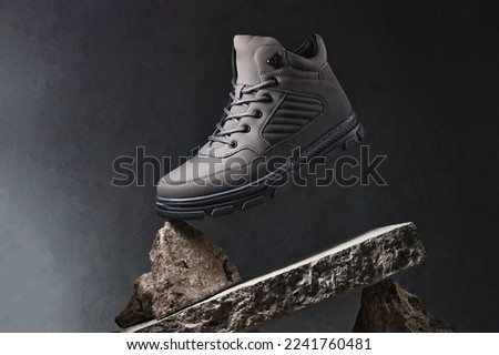 Male walking boots with stones or concrete block on gray background. Autumn stylish leather shoes for adventure or travel.