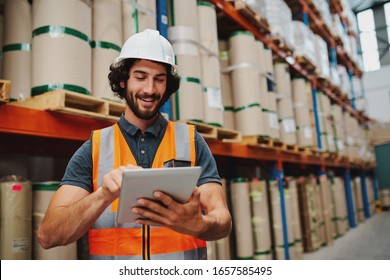 Male warehouse manager adding stock inventory data in digital tablet in warehouse wearing a white hardhat and safety vest standing