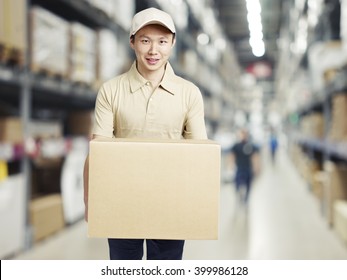 Male Warehouse Worker Carrying A Carton Box Of Goods In A Cash And Carry Wholesale Store.