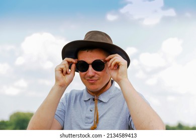 Male Wearing Black Sunglasses. Portrait Of Farmer With Blue Sky In Background. Young Man Wearing Sunglasses And Cowboy Hat In Field. Closeup. Happy Young Person.