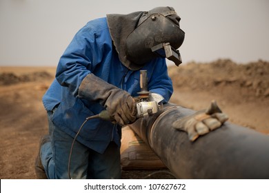 Male Welder Worker Wearing Protective Clothing Fixing Welding And Grinding Industrial Construction Oil And Gas Or Water Plumbing Pipeline Outside On Site