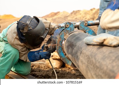 Male welder worker wearing protective clothing fixing and joining industrial construction oil and gas or water plumbing pipeline using an external pipe clamp outside on site