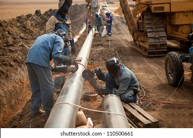 Male welder worker wearing protective clothing fixing welding and grinding industrial construction oil and gas or water and sewerage plumbing pipeline outside on site