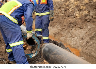 Male welder workers wearing protective high visibility clothing fixing and joining industrial construction oil and gas or water plumbing pipeline using an external pipe clamp outside on site