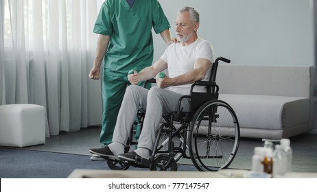 Male In Wheelchair Pumping His Weak Muscles With Help Of Nurse, Rehabilitation