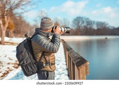 Male Wildlife Photographer In Park Taking Photo During Winter Time With Blue Sky And Snow On The Ground With Camouflage Clothes 