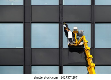 Male window cleaner cleaning glass windows on modern building high in the air on a lift platform. Worker polishing glass high in the air - Powered by Shutterstock