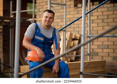 Male Worker In Blue Construction Overalls Resting At The Workplace. High Quality Photo