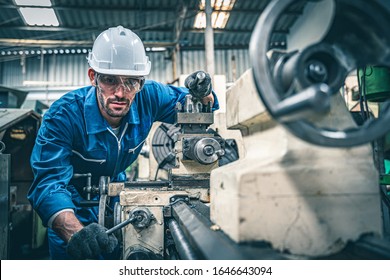 Male worker in blue jumpsuit and white hardhat operating lathe machine. 