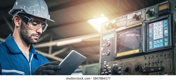 Male Worker In Blue Jumpsuit And White Hardhat Inspecting The Machine With Tablet Device.	
