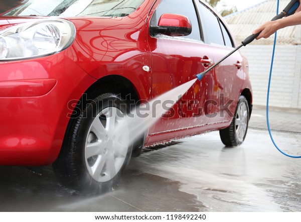 Male worker cleaning vehicle with high pressure\
water jet at car wash
