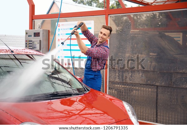 Male worker cleaning vehicle with high pressure\
water jet at car wash
