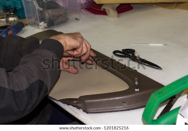 A male worker does manual work on skinning a\
genuine leather of a vehicle\'s interior with a beige-colored door\
to carry out a design solution in a car repair shop at the\
workplace with scissors