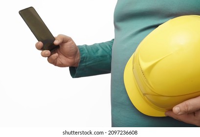 Male Worker Or Engineer Holding In Hands Yellow Safety Helmet And Cellphone Isolated On White Background. No Face.