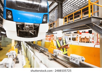 Male worker engineer standing diligently recording data tablet in front of electric locomotive at modern maintenance station preventative quality inspection rail system equipment safety before use. - Powered by Shutterstock