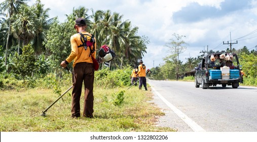Male worker with grass cutter / brush cutter cut grass at road side. Gardening concept.