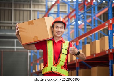 Male worker in hardhat holding cardboard box walking through in retail warehouse, Warehouse worker working in factory warehouse, Man carrying box and showing thumbs up