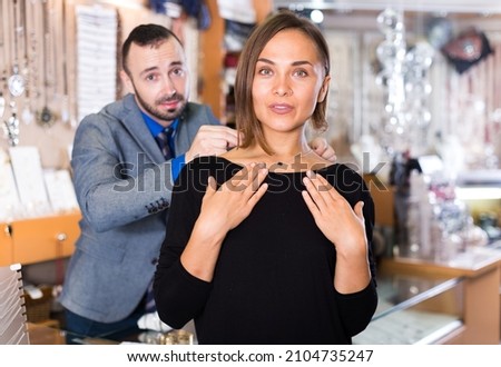 male worker helps to trying chainlet with pendants in the jewelry shop.