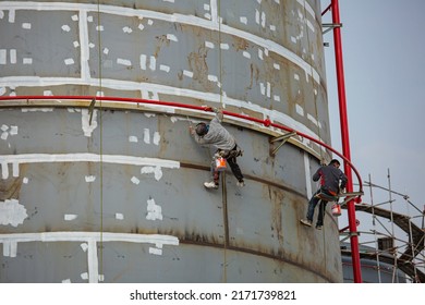 Male Worker Industrial Rope Access Worker Hanging From Tank Oil Shell Plate While Painting The Exterior.
