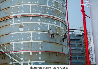 Male Worker Industrial Rope Access Worker Hanging From Tank Oil Shell Plate While Painting The Exterior.