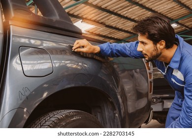 Male worker inspecting pickup truck, paint mechanic examining scratched car surface body damage near wheel arches using white chalk to paint circles to repair in auto workshop factory with insurance.
 - Powered by Shutterstock