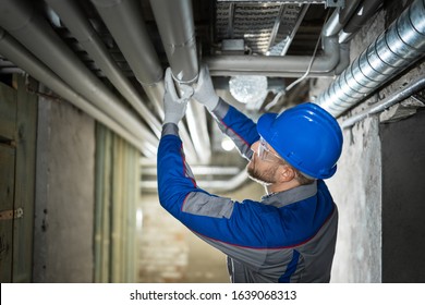 Male Worker Inspecting Water Pipes For Leaks In Basement