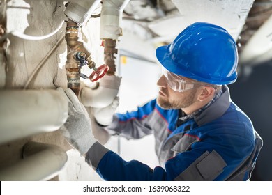 Male Worker Inspecting Water Valve For Leaks In Basement