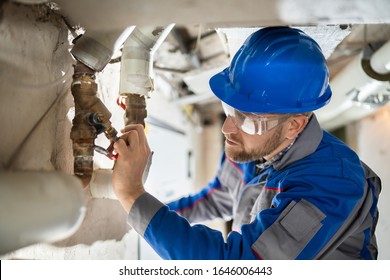 Male Worker Inspecting Water Valve For Leaks In Basement