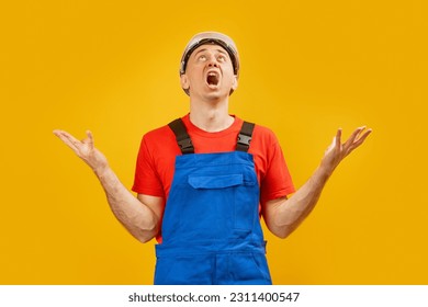 Male worker looks up in surprise. Middle-aged man wears industrial engineer clothes throws up his hands in despair and screams. Copy space. - Shutterstock ID 2311400547