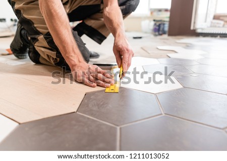 Male worker makes measurements and installing new wooden laminate flooring. The combination of wood panels of laminate and ceramic tiles in the form of honeycomb. Kitchen renovation.