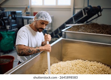 Male worker mixing popcorn in processing machine in a factory.