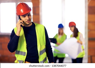 male worker on a residential construction site talking on his phone. his team of engineers working in the background