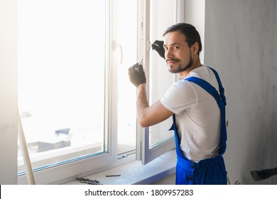 Male worker in overalls installs a window and poses at the camera