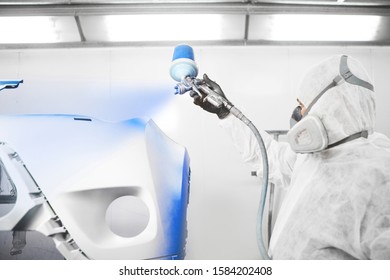 Male Worker Painting A Car Bumper In A White Paint Booth.