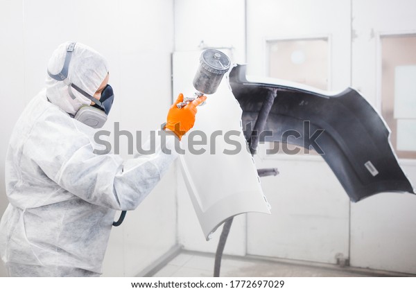 Male worker\
painting a car in a white paint\
booth.