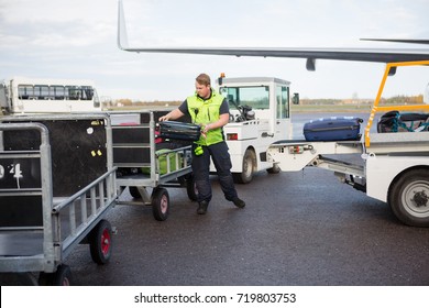 Male Worker Placing Luggage In Trailer On Runway